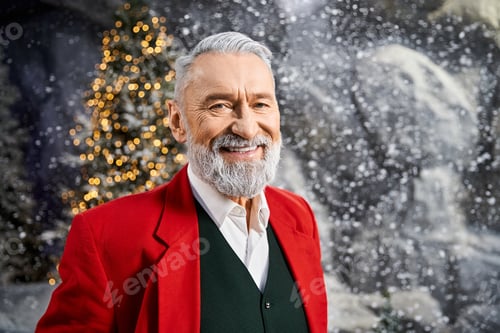 Preview: Festive man in a bright red jacket smiles against a snowy Christmas backdrop with a tree