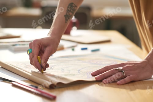 Preview: Hands of young creative woman with yellow crayon drawing on paper