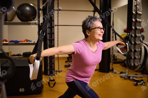 Preview: Adult smiling caucasian woman doing sport exercise with hanging sport ropes