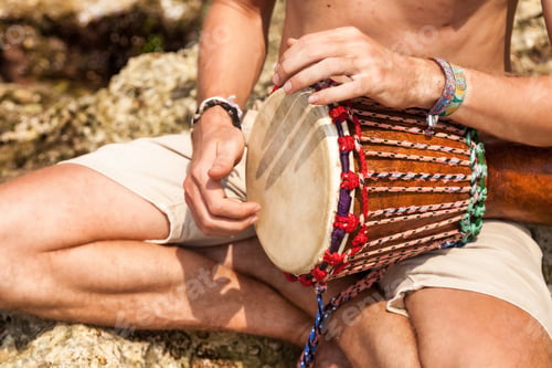 Preview: Close up hands young man drummer, playing rhythm with djembe drum, sitting at tropical