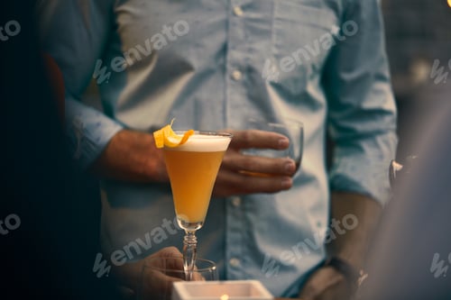 Preview: Closeup shot of a beautiful yellow cocktail and a person holding a glass of whiskey