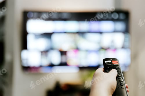 Preview: Hand holding remote control pointing to TV. Person watching smart television