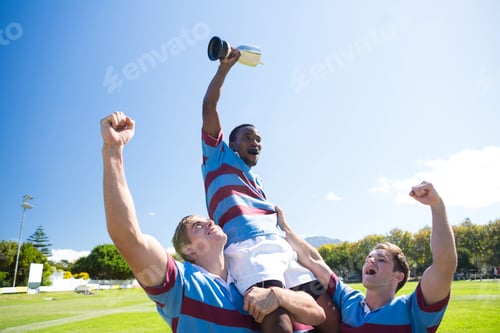 Preview: Happy rugby team enjoying victory while standing at field against sky