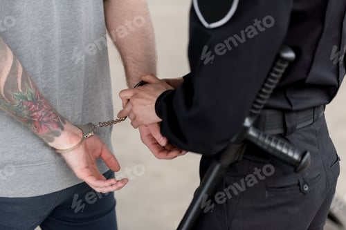 Preview: cropped shot of policewoman with truncheon handcuffing bandit