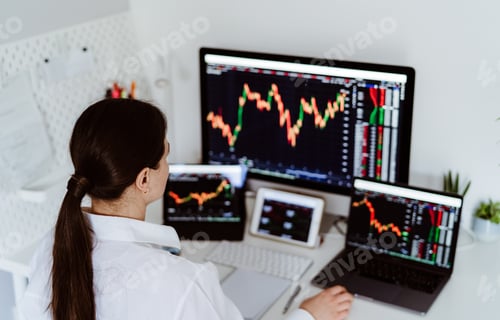 Preview: Back view of young female cryptocurrency investor sitting at desk looking at multiple screens