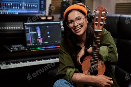 Preview: Portrait of beautiful young brunette, female artist smiling at camera while sitting with ukulele in