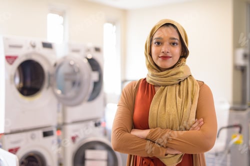 Preview: Young beautiful Indian Muslim businesswoman with arms crossed as owner of the laundromat