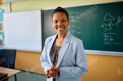Preview: Happy black teacher in front of chalkboard at school looking at camera.