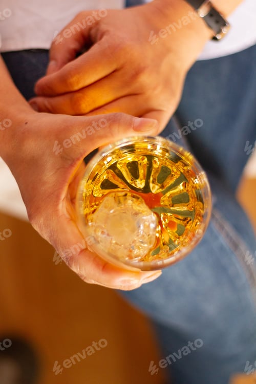 Preview: Vertical top of a female wearing jeans while holding a glass of whisky