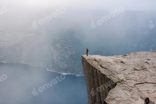 Preview: A lone hiker stands on the precipice of a dramatic cliff in Norway,Preikestolen, Norway