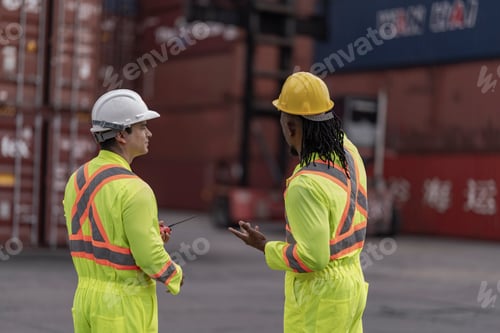 Preview: Two workers in reflective suits walk through a container yard, overseeing logistics