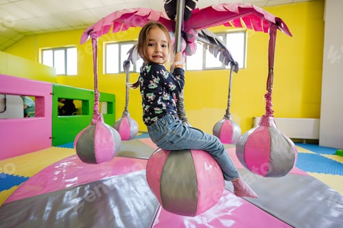 Preview: Happy girl playing at indoor play center playground, swing on palm.