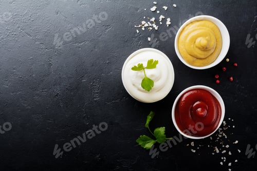 Preview: Set of three sauces - mayonnaise, mustard and ketchup in white ceramic bowls on black stone or concr
