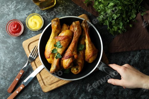 Preview: Female hand hold frying pan with roast chicken drumsticks