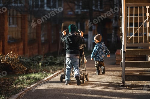 Preview: boys are walking on the street. The eldest brother rolls the youngest in a stroller