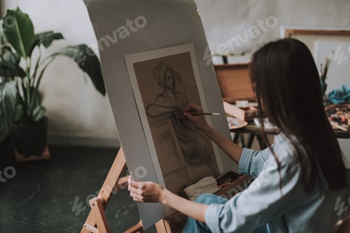 Preview: Talented Female Artist Drawing A Woman While Sitting In The Art Studio In Front Of The Easel