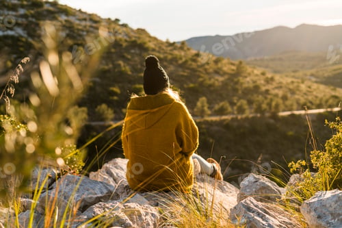 Preview: Young woman sitting on rock in nature looking at view