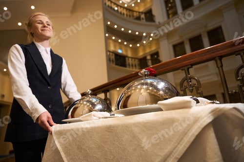 Preview: Joyful waitress carries serving cart along corridor of chic hotel