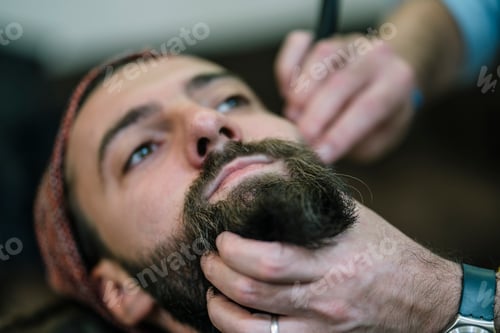 Preview: Man arranging his beard in modern barbershop.