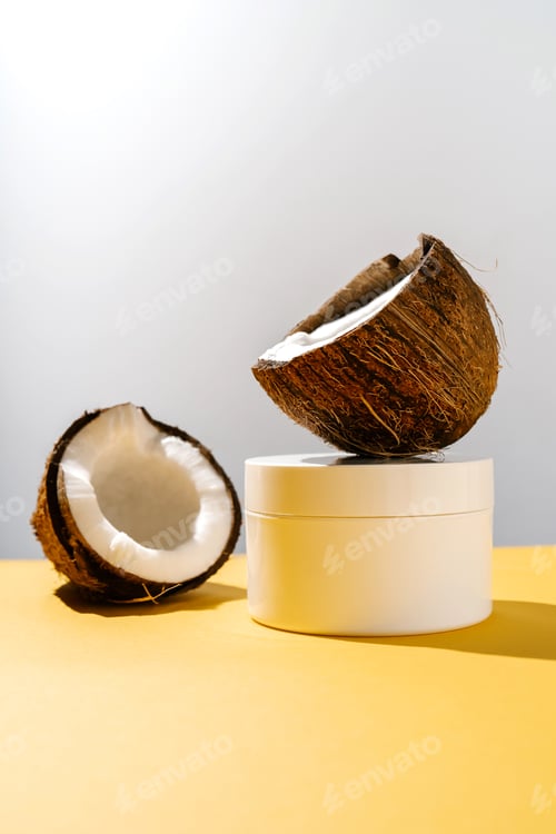 Preview: Two halves of coconut and a jar of cosmetics on a yellow and gray background.