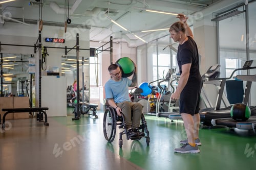 Preview: Spinal injury rehab with personal trainer. Wheelchair man lift weighted ball for upper body health