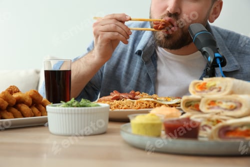 Preview: Food blogger eating in front of microphone at table against light background, closeup. Mukbang vlog