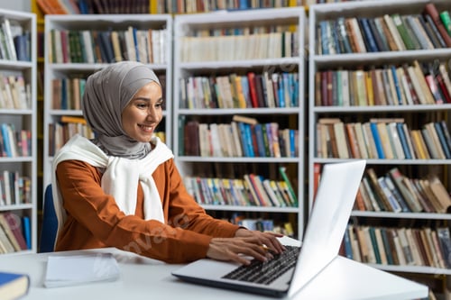 Preview: Young beautiful student in hijab studying online remotely in university library, woman typing on