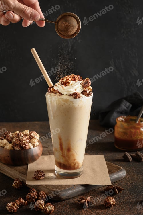 Preview: Tasty banana and caramel milkshake garnished whipped cream and popcorn on dark brown background.