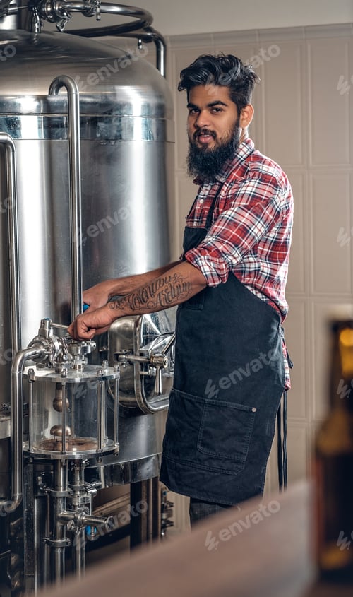 Preview: Indianr male manufacturer presenting craft beer in the microbrewery.