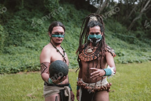 Preview: Group of ethnic Mayan male warriors in traditional accessories and face painting looking at camera