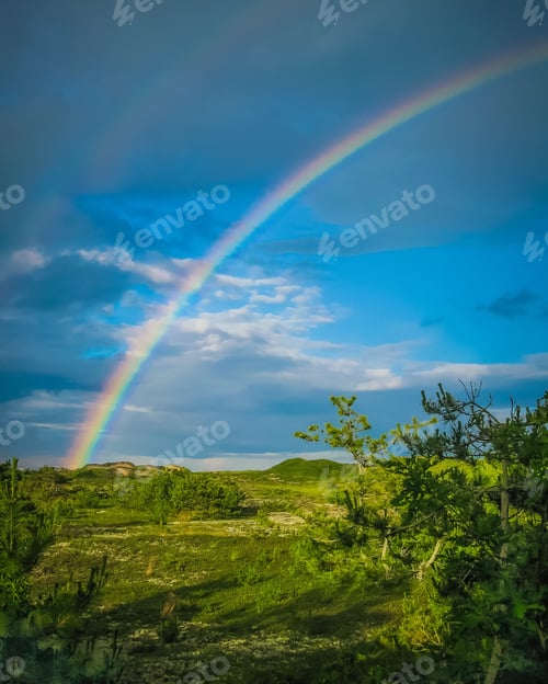 Preview: Post storm double rainbow in a blue sky over green landscape .