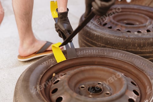 Preview: An unrecognizable man uses a crowbar to disassemble a car tire.