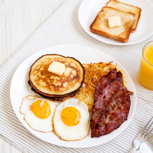 Preview: Full American Breakfast with Bacon, Hash Browns, Eggs and Pancakes on a plate on a white wooden