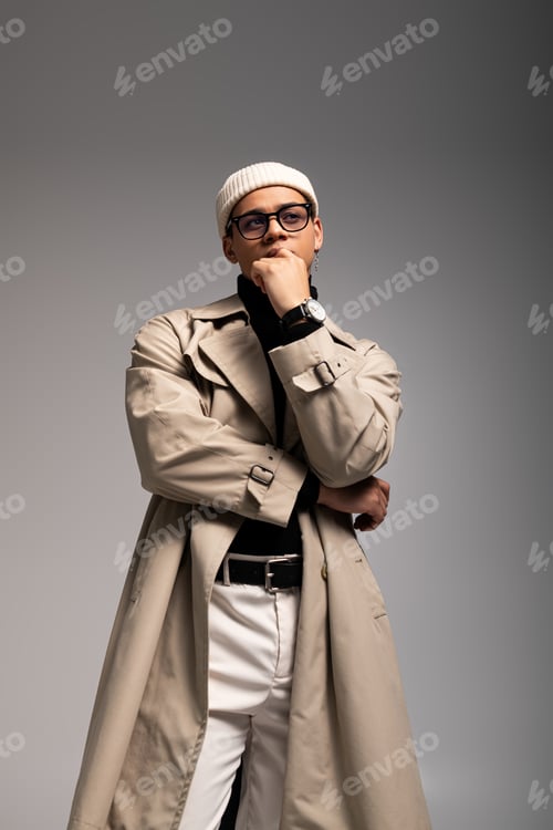 Preview: Young man in stylish trench coat and hat poses confidently with a thoughtful expression