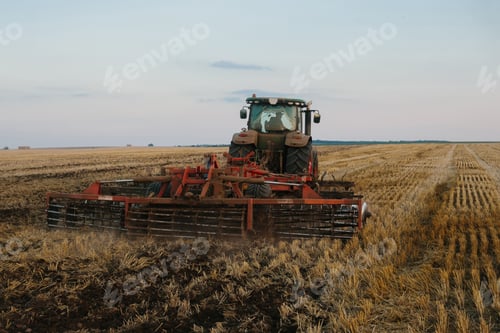 Preview: Modern tractor with a heavy trailed disc harrow works a wide hilly field.