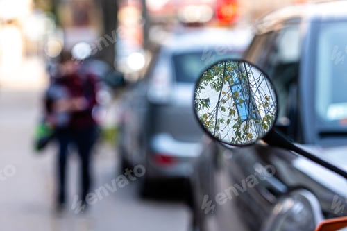 Preview: close-up of a motorcycle mirror parked on the side of the street, soft focus, blurred background