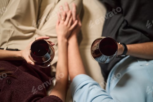 Preview: Young Couple Holding Hands and Drinking Red Wine Together Indoors