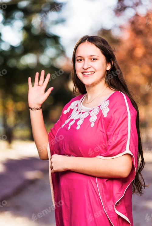 Preview: Moroccan young woman waving and greeting looking at camera with traditional Arab dress