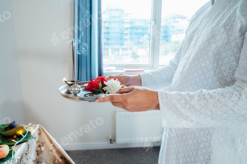 Preview: Close up Indian man holding pooja ki thali engages in worship at home altar for god Ganesh