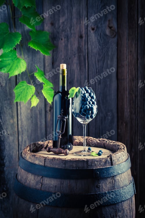 Preview: Ripe red grapes in glass and wine on old barrel