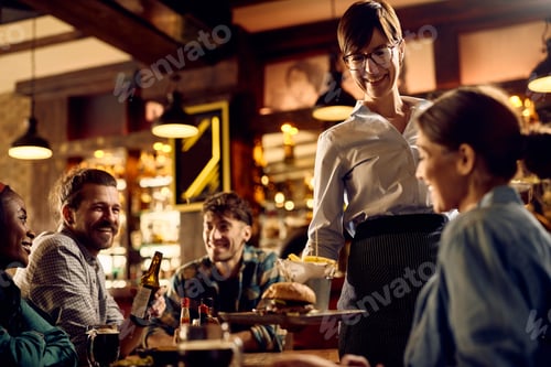 Preview: Happy waitress serving food to guests in a pub.