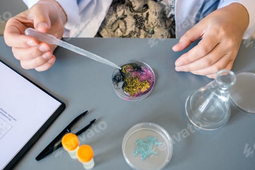 Preview: Female scientist adding drop of liquid from from pipette over petri dish with mix of glitters in lab