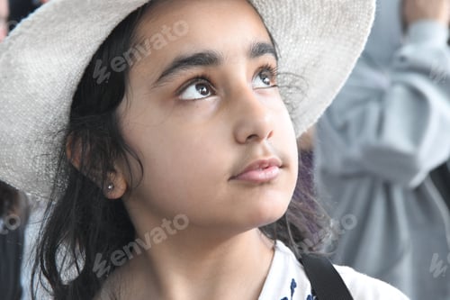 Visualização: Jovem menina paquistanesa asiática com um chapéu branco olhando melancolicamente