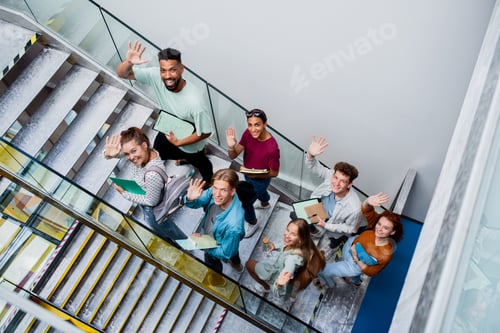 Preview: Top view of university students walking up the stairs indoors, looking at camera and waving