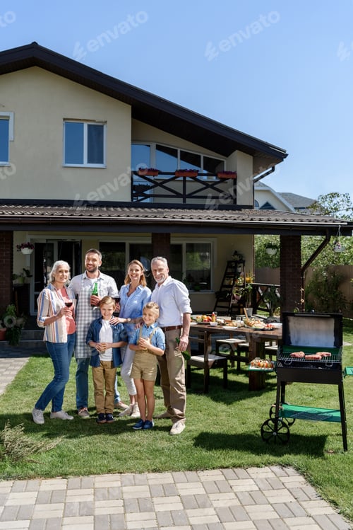 Preview: Happy family of three generations standing together on green lawn and smiling at camera