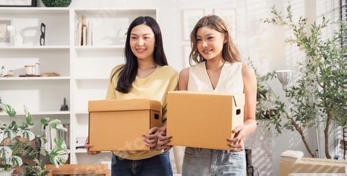Preview: Happy Asian girl friends holding cardboard boxes moving to the new home