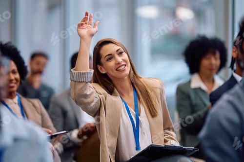 Preview: Happy entrepreneur raising her arm to ask a question during business conference in board room.