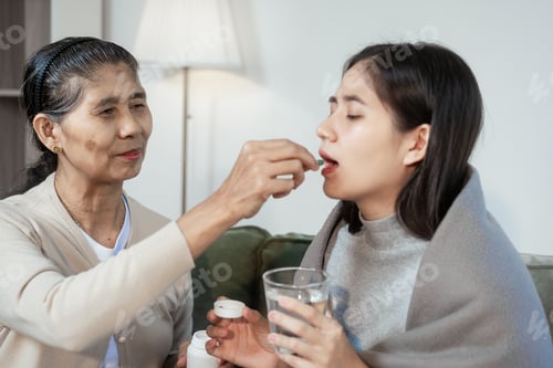 Preview: An elderly Asian woman gently checks her sick daughter's forehead, offering care and comfort