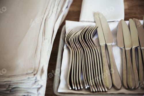 Preview: High angle close up of napkins and silver forks and knives on a table in a restaurant.