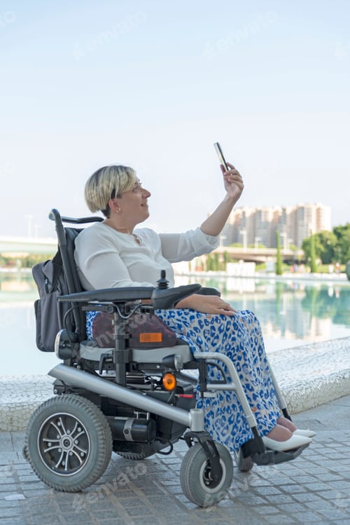 Preview: vertical portrait of a woman with disability in a wheelchair taking a selfie photo in the city